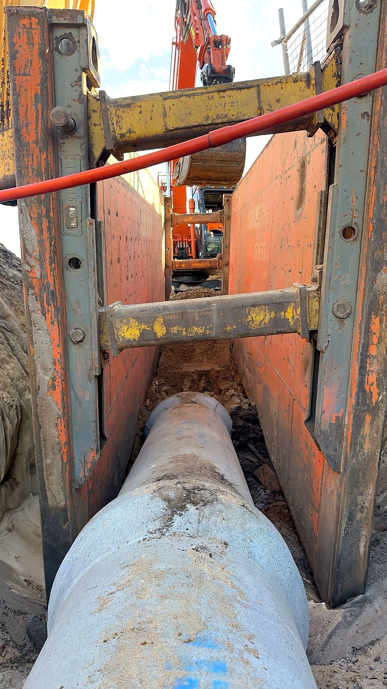 A concrete stormwater pipe laid in a shored trench, with an excavator at the head of it
